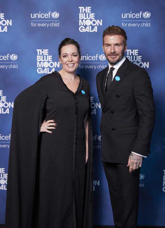 Olivia Colman and David Beckham standing in front UNICEF's Blue Moon Gala display boards